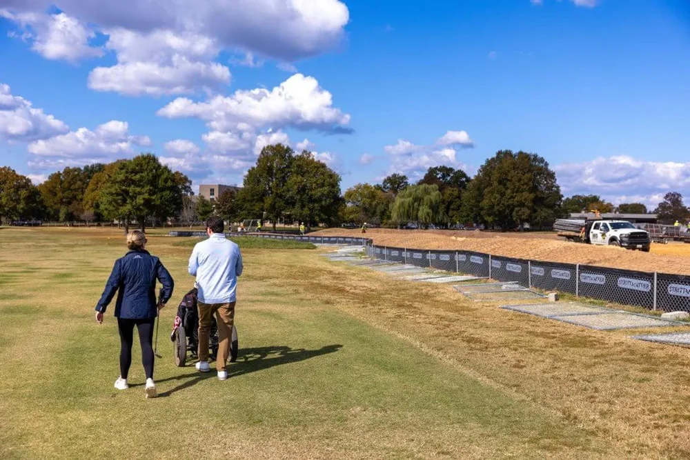 Golfers walk to a hole at East Potomac Golf Links as trucks unloads debris and soil from the demolition of the White House's East Wing.
